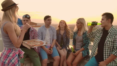 Die-Gruppe-Von-Sechs-Jungen-Leuten-Kommuniziert-Auf-Dem-Dach-Bei-Pizza-Und-Bier-Miteinander.-Mädchen-Genießt-Den-Duft-Heißer-Pizza.